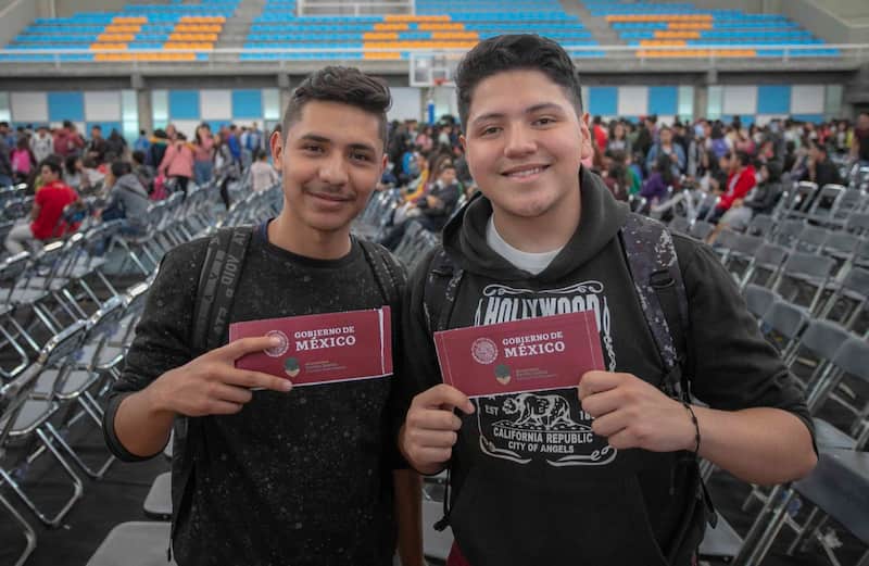Aquí te decimos de cuánto será el monto del pago de la beca Benito Juárez y de la Rita Cetina Dos jóvenes recogiendo su tarjeta de la beca Benito Juárez